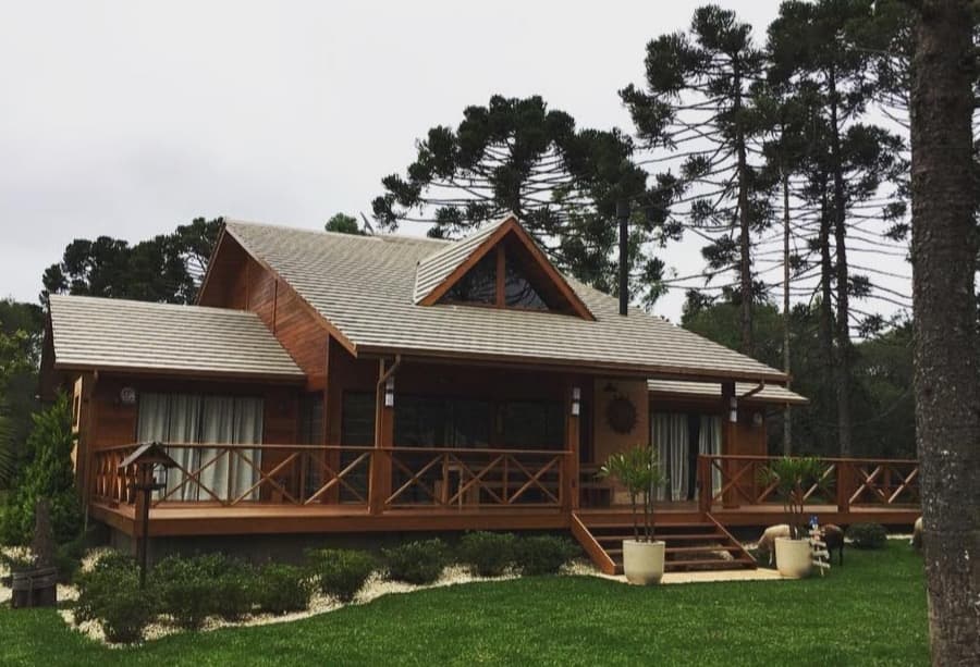 Casa de madeira com varanda, jardim e araucárias, realizada pela empresa